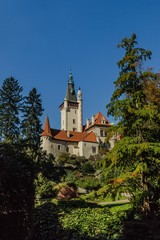 Fototapeta premium Pruhonice, Czech Republic - October 7 2019: Scenic view of famous romantic castle standing on a hill surrounded with tall green trees. Sunny autumn day with blue sky. Vertical image.