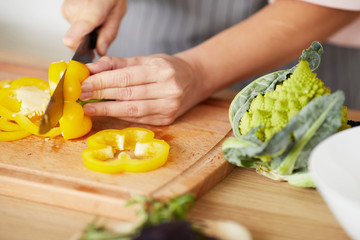 Close-up of woman cutting yellow fresh pepper with knife on cutting board she preparing dinner