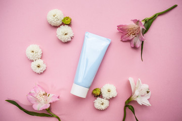 A blue tube of cosmetic product with a white cap on a pink background with alstroemeria and other colors.