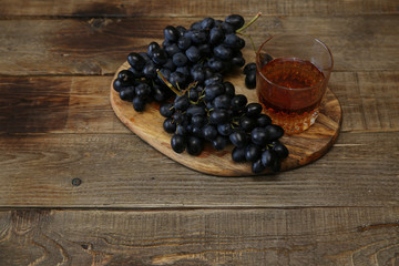 glass of brandy or wine and a juicy bunch of black grapes on a wooden rustic table. With copy space for text.