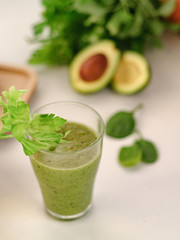Green smoothie with a stalk of celery in a glass cup. On the table is an avocado.