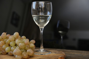 Fototapeta premium glass of white wine and bunch of grapes with reflection in glass on a wooden table