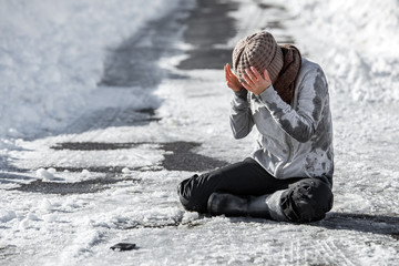 Frau hält sich den Kopf, Verletzung durch Glatteis und Schnee auf der Straße im Winter