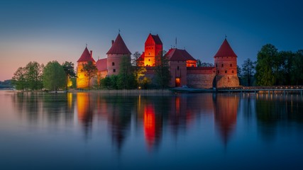 Naklejka na ściany i meble Beautiful medieval castle with red roofs and brick walls reflecting in calm lake at night. Travel destinations