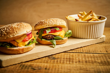 two tasty burgers and fries on wooden board and black background