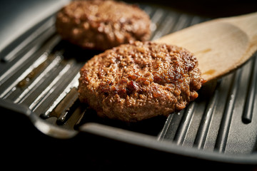 Closeup of juicy burgers fried on black grill pan