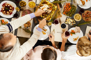High angle view of man cutting roast turkey with knife while have holiday dinner together with his...
