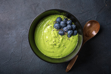 Overhead shoot of breakfast detox green smoothie bowl from banana and spinach on black background. Healthy food concept with copy space, top view