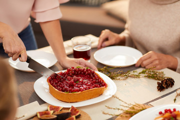 Close-up of woman cutting sweet berry pie with kitchen knife on the table and treating her guests