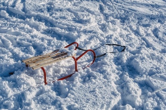 sanki na śniegu, drewniane siedzenie i czerwone płozy sanek dla dzieci