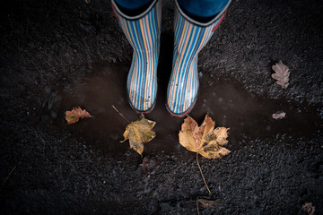 A woman wearing rubber boots jumps into a puddle on a cold autumn day.