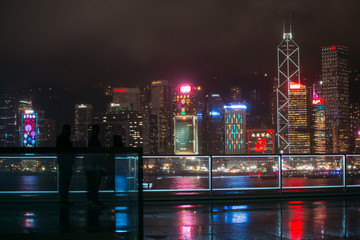 People stand in front of Victoria Harbor, Hong Kong at raining night