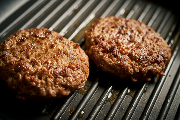 Closeup of juicy burgers fried on black grill pan