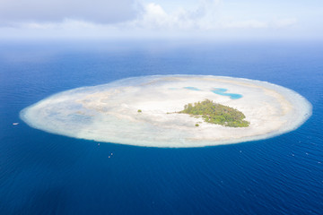 Obraz premium The idyllic island of Pulau Midorang is surrounded by a circular coral reef in the blue waters of the Ceram Sea, Indonesia. This remote site is a beautiful destination for scuba diving and snorkeling.