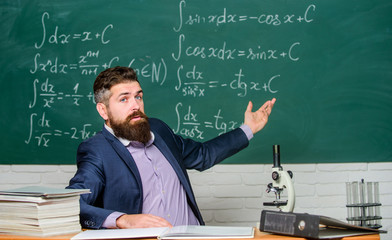 Talking to students or pupils. School teacher concept. Teacher bearded man tell interesting story. Teacher charismatic hipster sit at table classroom chalkboard background. Educational conversation