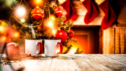 A wooden table with space for your advertising products. Blurred great green Christmas tree and Fireplace with flames and red socks of Santa Claus background.