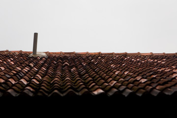 Tiled roof and chimney against the background of an uninformative cloudy sky.