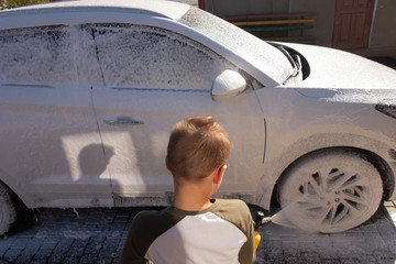 A middle-aged man teaches children of boys 4 and 10 years old to wash a car in the yard of his...