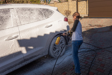 A middle-aged man teaches children of boys 4 and 10 years old to wash a car in the yard of his...