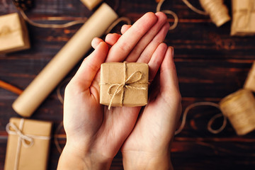Obraz premium Women's hands hold a gift of craft paper. Against the background of dried orange, cinnamon, pine cones, anise on a wooden table.