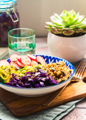 Buddha bowl with rainbow colors ingredients - avocado, fermented red cabbage, quinoa, radish, green beans, sesame and pumpkin seeds. Dish served on wooden board. Healthy vegan plant based lunch.