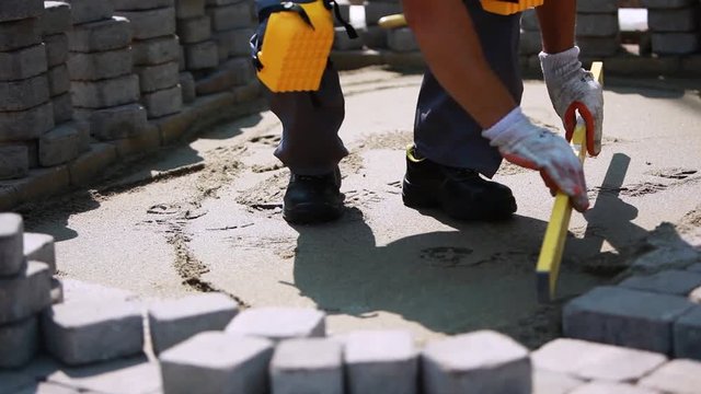Stone Pavement Road Construction Workers. Using Bubble To Level The Sand Surface