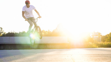 Young BMX biker jumping bunny hop tricks in sunny park in summer afternoon with lens flare