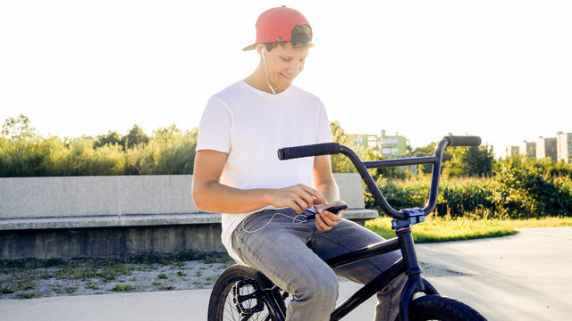 Portrait of happy handsome bmx rider using mobile phone while riding a BMX bike smiling messaging friends via social networks - Powered by Adobe