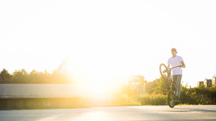 Young male fooling around with BMX bike in city park on sunny summer summer afternoon