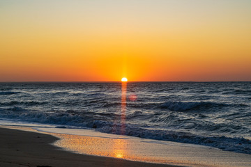 Sunrise over the Black sea, waves on the sandy beach.