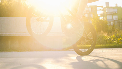 Close up of BMX biker riding manual wheelie trick in sunny park on beautiful summer day with lens...