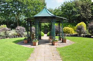 Large  hexagonal gazebo provides shade for seating inEnglish formal garden 