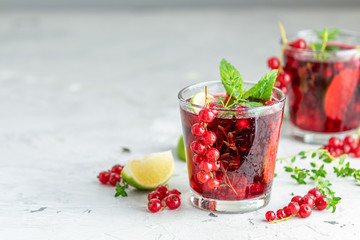 Cold red cocktail with currant, lime, mint, thyme and ice in glass on light gray concrete surface table. Summer drinks and alcoholic cocktails. Alcoholic cocktail Currant mojito.