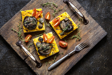 polenta corn with fried eggplant and mushrooms and cherry tomatoes on a dark background