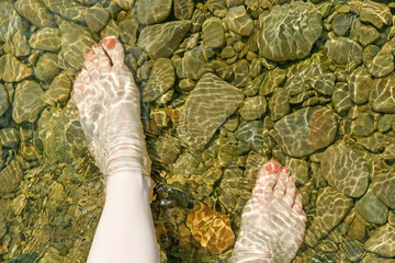 Feet of a woman walking in a shallow river.