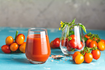 Glasses of fresh delicious jummy red tomato juice and fresh raw tomatoes with pink salt in spoon on light concrete surface. Close up. Gmo free. Natural good food