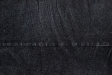 Texture of a black denim fabric. Two pieces of fabric stitched together