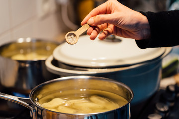 une main tient une cuillère pour épicer un plat en cuisine dans une casserole 