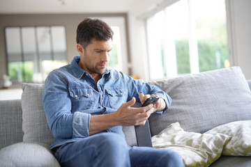 Man at home relaxing in sofa, using smartphone