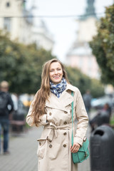 Fototapeta premium Happy young adult woman smiling outdoors and walking on city street wearing autumn clothes and scarf