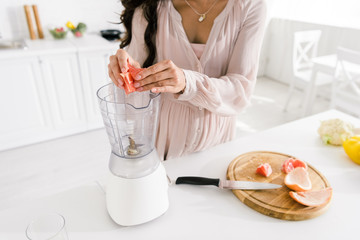 cropped view of pregnant woman putting sliced grapefruit in blender