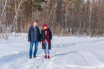 Handsome man and attractive young woman walking along snowy country road in sunny day. Beautiful look, male and female fashion, winter outfit. Winter holidays, weekend at countryside concept