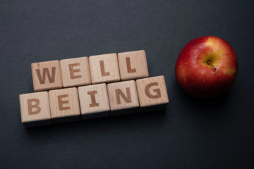 Wooden block form the word WELL BEING and apple, health concept.