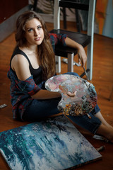 Naklejka premium Portrait of young talented artist with palette in workshop surrounded by paintings
