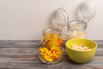 Homemade sauerkraut in glass jars with open lids and salad bowls on a wooden background. Rustic style