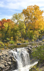 Vibrant orange, yellow, red and green fall colors on trees near waterfall