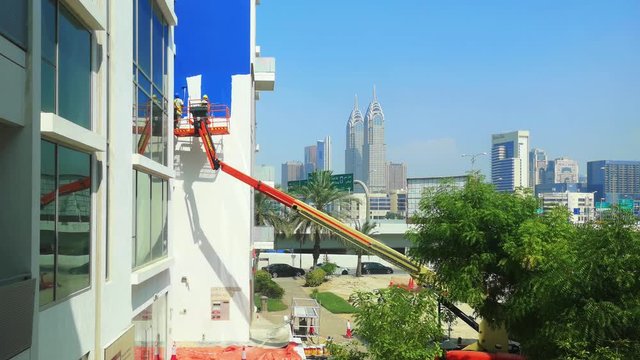 Workers painting the exterior of a building using a crane - construction site and tools for repair and home improvements