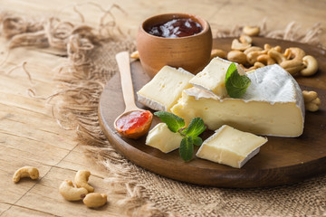 Brie type of cheese with jam. Camembert cheese. Fresh Brie cheese and a slice on a wooden board with nuts, honey and leaves. Italian, French cheese.
