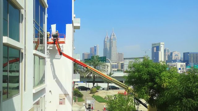 Workers painting the exterior of a building using a crane - construction site and tools for repair and home improvements