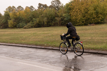 Girl in a jacket with a hood rides a bicycle in rainy weather